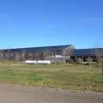 A coffee brown post-frame equestrian riding arena with open lean-to front porch