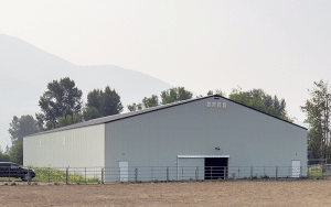A bone white post-frame equestrian riding arena with sliding doors, and a overhead door
