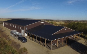 A coffee brown post-frame equestrian riding arena with open lean-to front porch