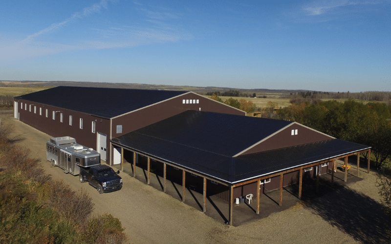 A coffee brown post-frame equestrian riding arena with open lean-to front porch