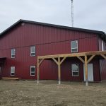 A dark red post-frame equestrian barn and office with open lean-to and deck