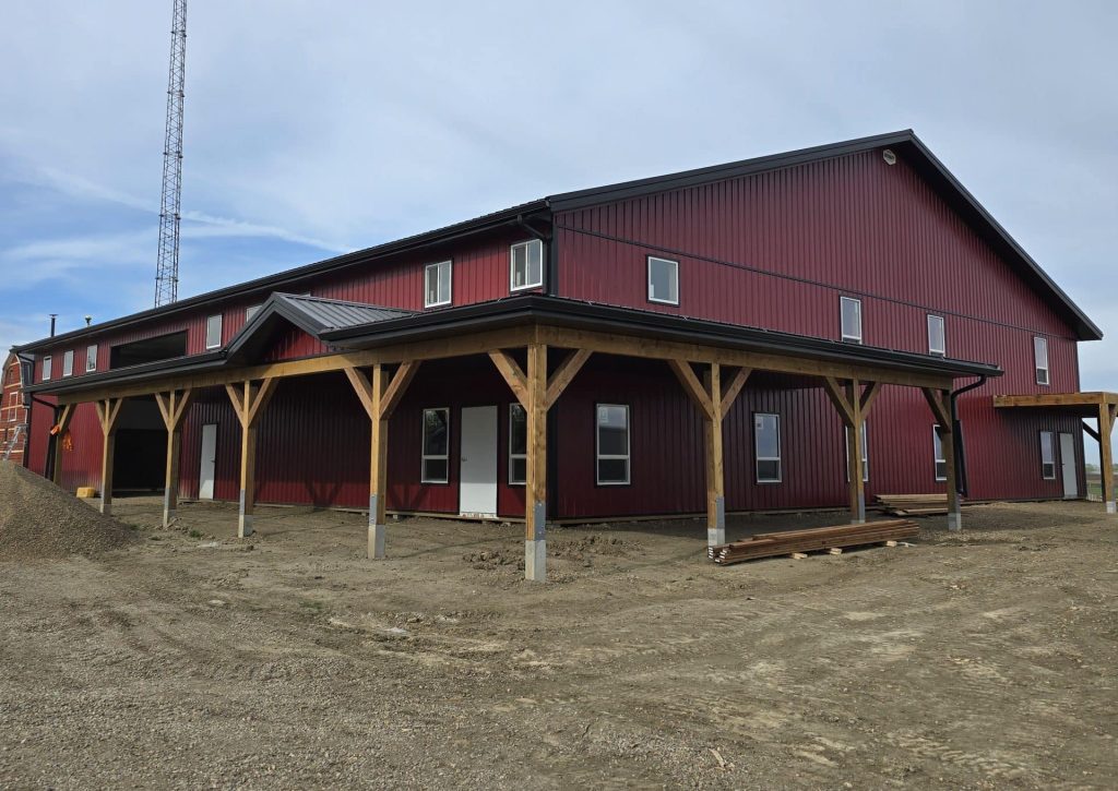 A dark red post-frame equestrian barn and office with open lean-to and deck