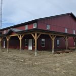 A dark red post-frame equestrian barn and office with open lean-to and deck