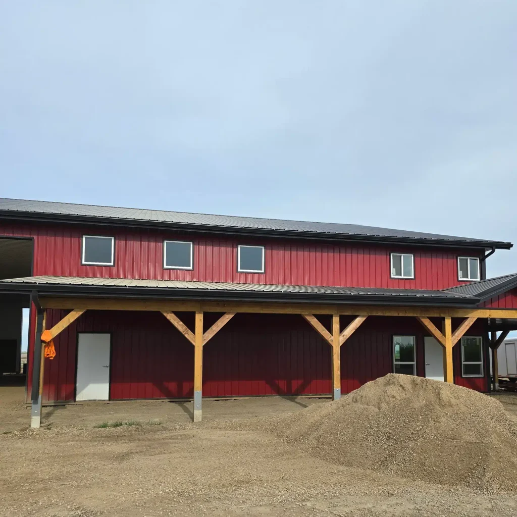 A dark red post-frame equestrian barn and office with open lean-to and deck