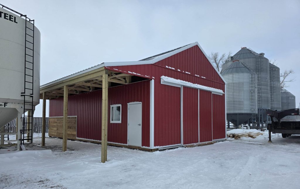 A post-frame red barn with exterior kick wall and a sliding door