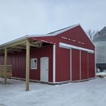 A post-frame red barn with exterior kick wall and a sliding door
