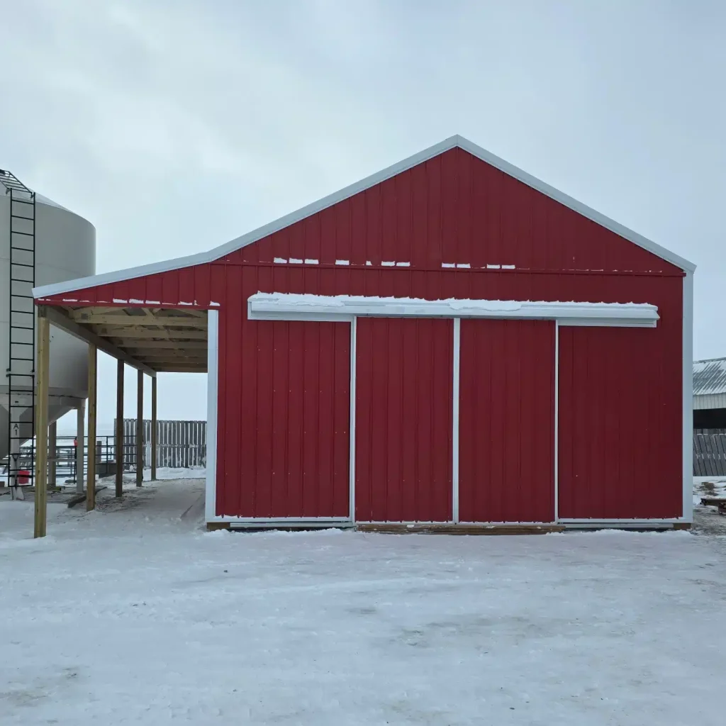 A post-frame red barn with exterior kick wall and a sliding door