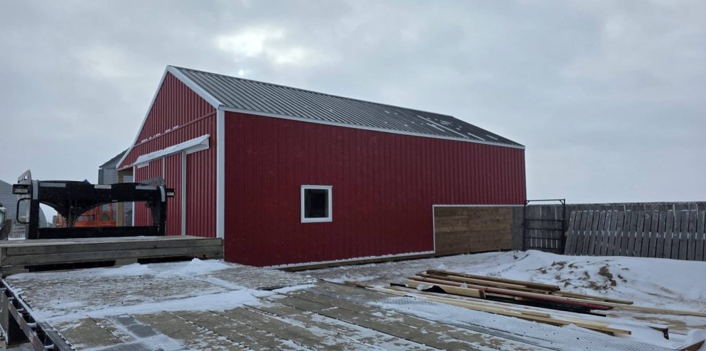 A post-frame red barn with exterior kick wall and a sliding door