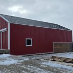 A post-frame red barn with exterior kick wall and a sliding door