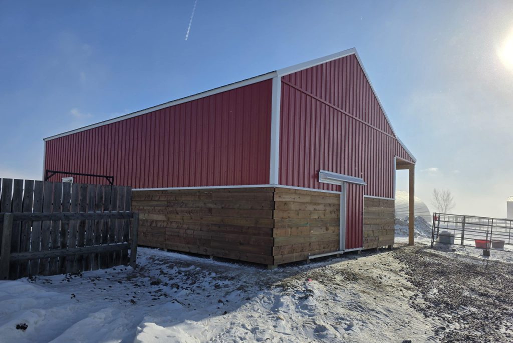 A post-frame red barn with exterior kick wall and a sliding door
