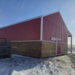 A post-frame red barn with exterior kick wall and a sliding door