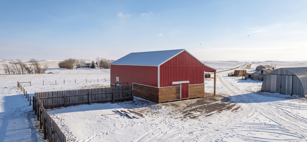 A post-frame red barn with exterior kick wall and a sliding door