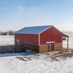 A post-frame red barn with exterior kick wall and a sliding door