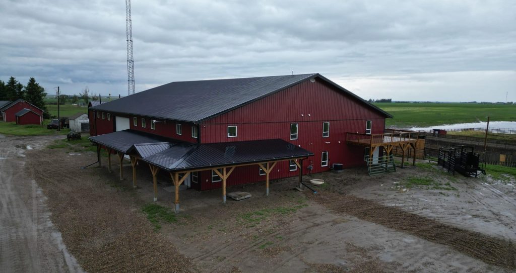 A dark red post-frame equestrian barn and office with open lean-to and deck