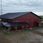 A dark red post-frame equestrian barn and office with open lean-to and deck