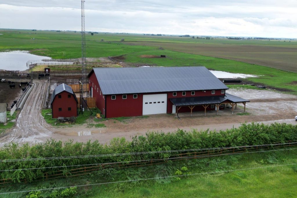 A dark red post-frame equestrian barn and office with open lean-to and deck