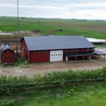 A dark red post-frame equestrian barn and office with open lean-to and deck