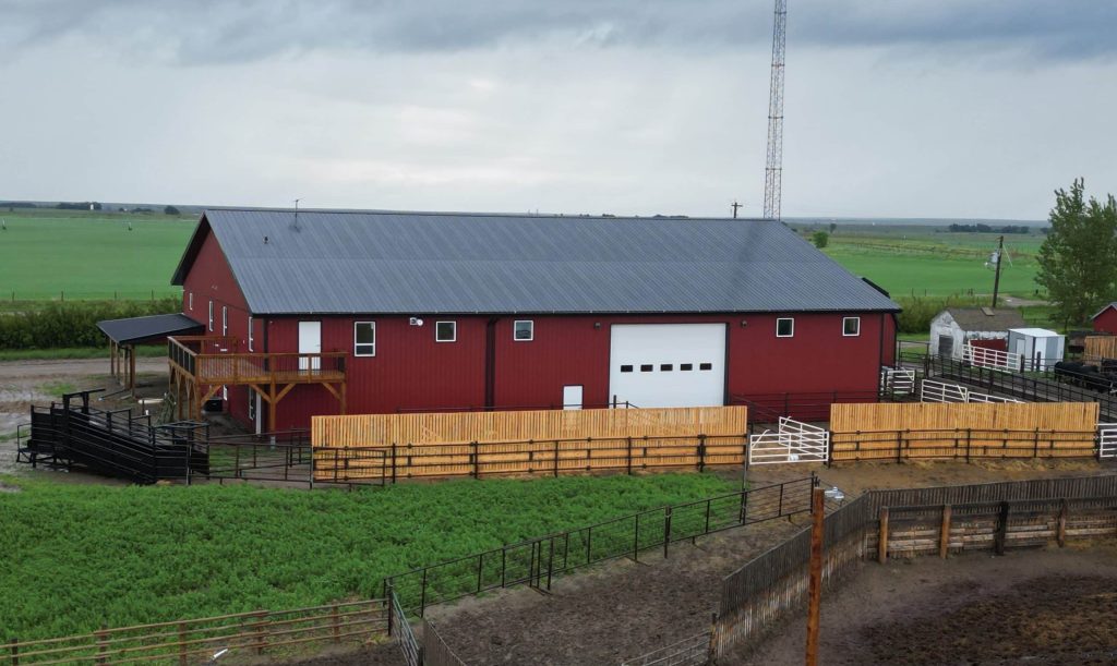 A dark red post-frame equestrian barn and office with open lean-to and deck