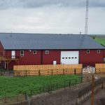 A dark red post-frame equestrian barn and office with open lean-to and deck