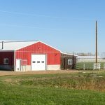 A dark red post-frame equestrian Shop with four overhead and four bi-fold doors