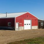 A dark red post-frame equestrian Shop with four overhead and four bi-fold doors