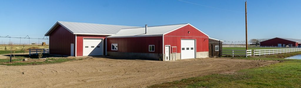 A dark red post-frame equestrian Shop with four overhead and four bi-fold doors