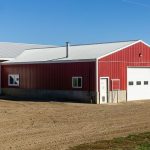 A dark red post-frame equestrian Shop with four overhead and four bi-fold doors