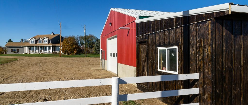 A dark red post-frame equestrian Shop with four overhead and four bi-fold doors