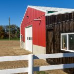 A dark red post-frame equestrian Shop with four overhead and four bi-fold doors