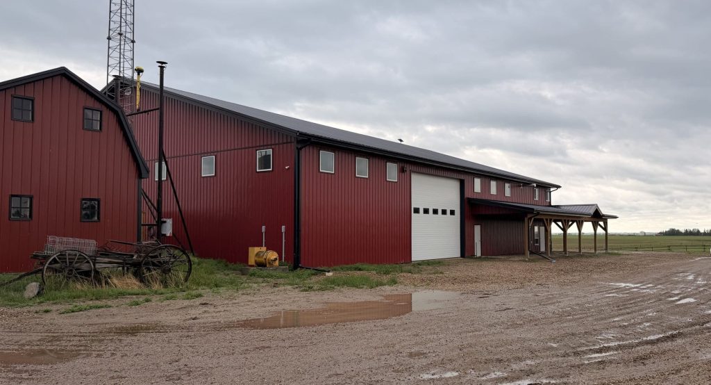 A dark red post-frame equestrian barn and office with open lean-to and deck