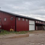 A dark red post-frame equestrian barn and office with open lean-to and deck