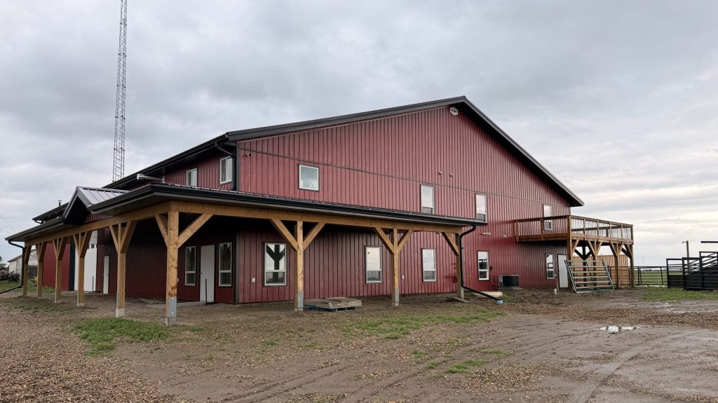 A dark red post-frame equestrian barn and office with open lean-to and deck