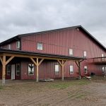 A dark red post-frame equestrian barn and office with open lean-to and deck
