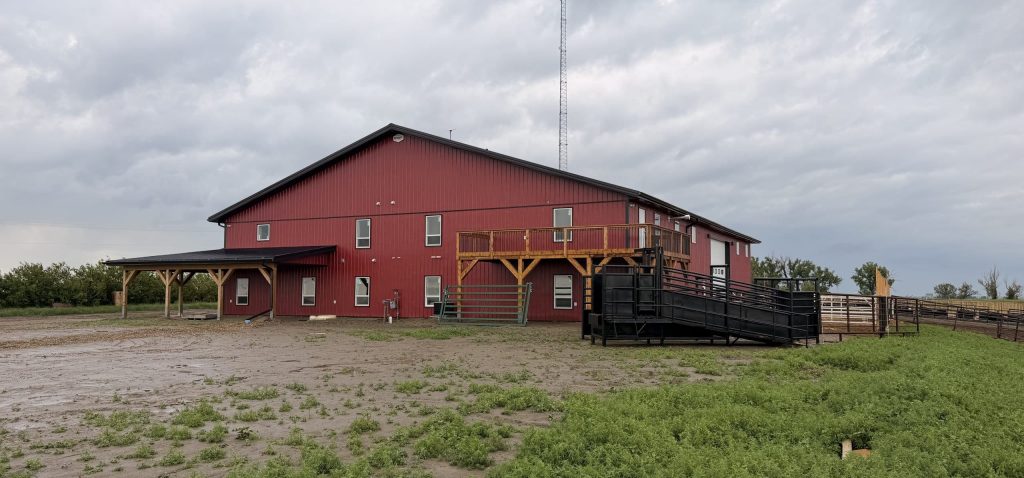 A dark red post-frame equestrian barn and office with open lean-to and deck