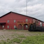 A dark red post-frame equestrian barn and office with open lean-to and deck