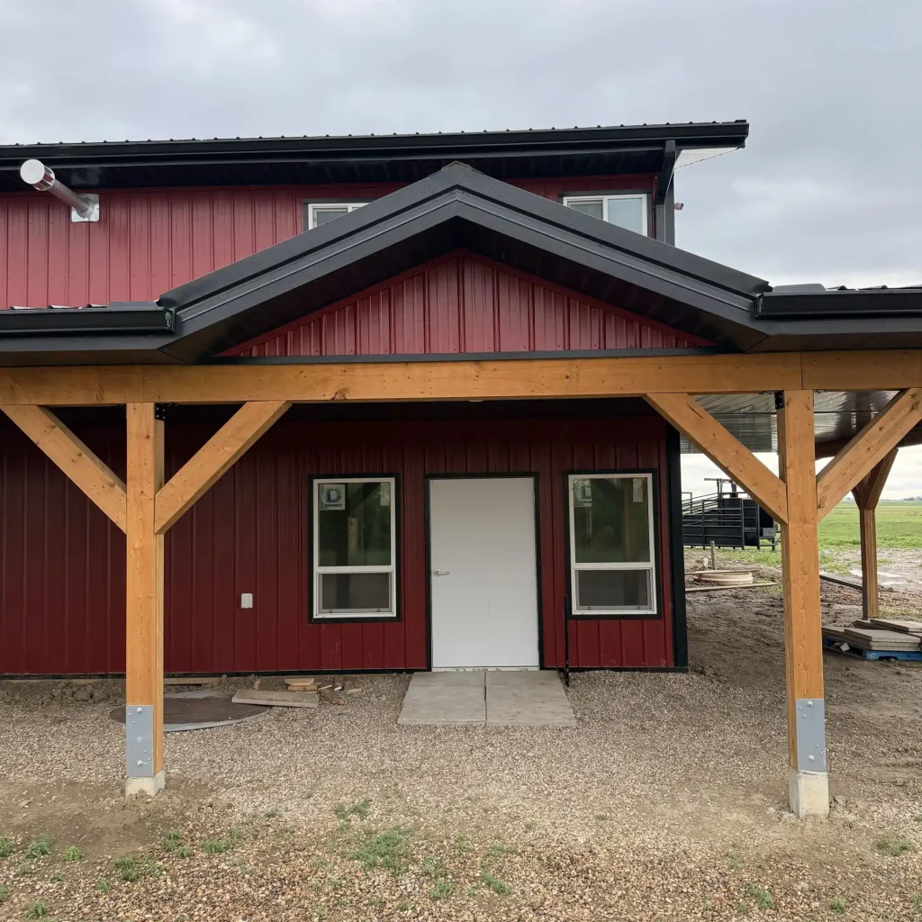 A dark red post-frame equestrian barn and office with open lean-to and deck