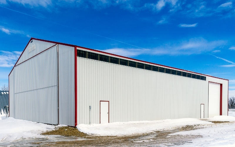 A white white post-frame agriculture machine shed with a bi-fold door and an overhead door