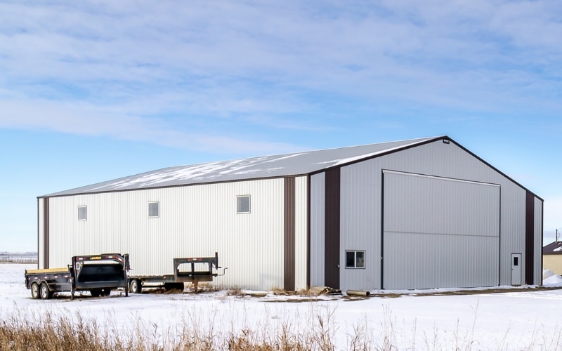 A white white post-frame agriculture machine shed with coffee brown trims and a bi-fold door