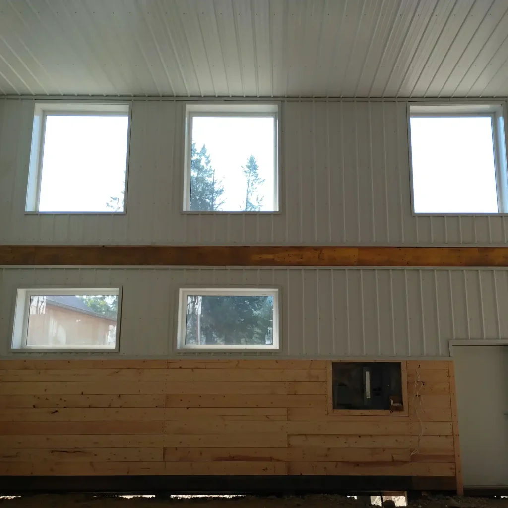 A bright white post-frame equestrian riding arena with black wainscoting