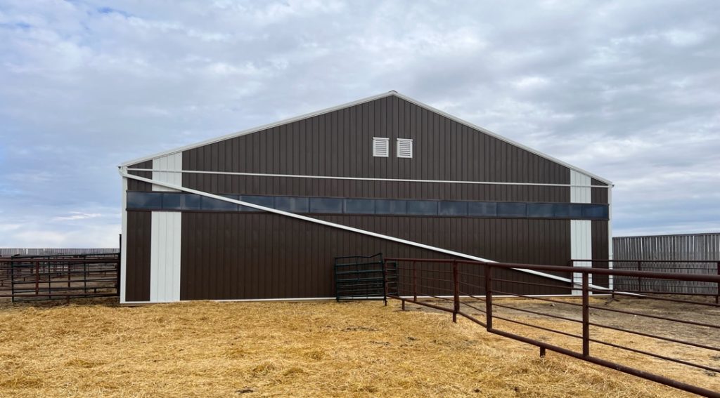 A coffee brown post-frame livestock shelter with overhead and sliding doors