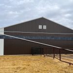 A coffee brown post-frame livestock shelter with overhead and sliding doors