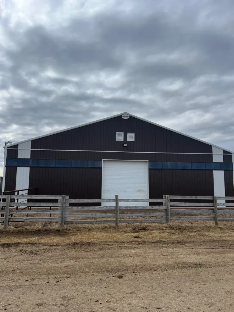 A coffee brown post-frame livestock shelter with wall lights and a sliding door