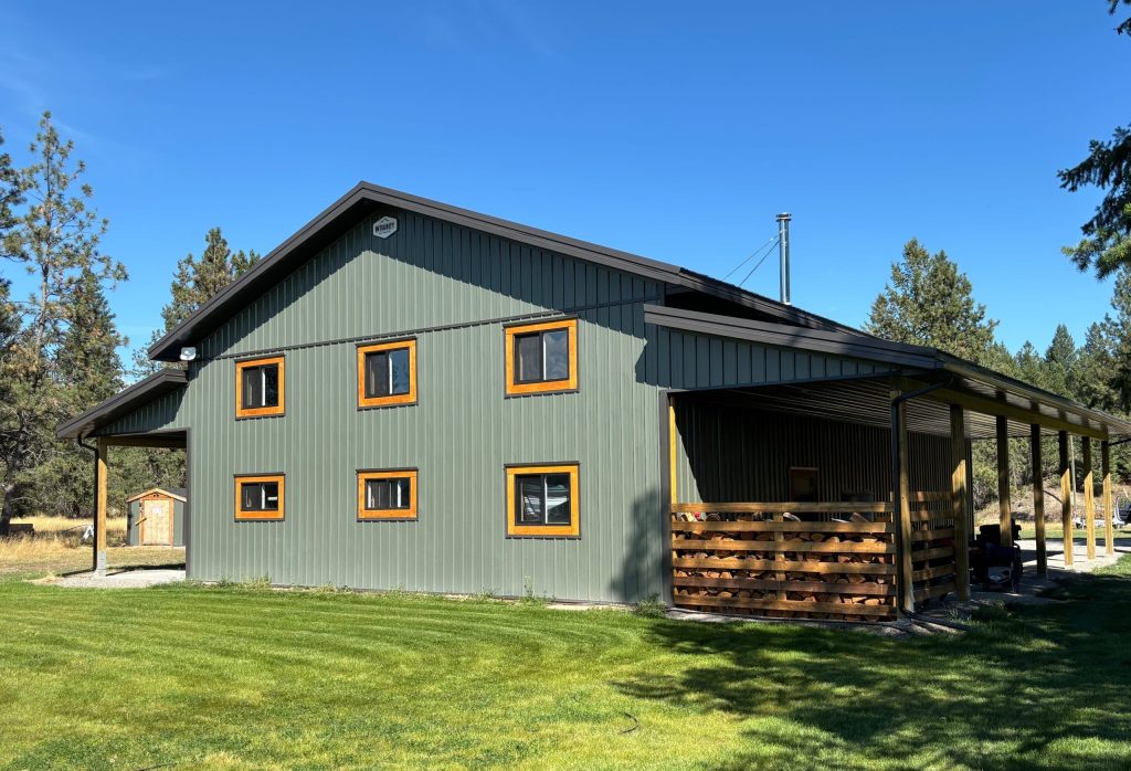 A dark sage post-frame shop with open lean-tos, soffits, and wooden trims