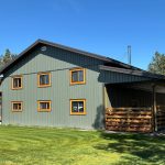 A dark sage post-frame shop with open lean-tos, soffits, and wooden trims