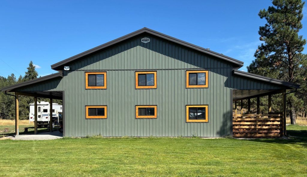 A dark sage post-frame shop with open lean-tos, soffits, and wooden trims