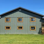 A dark sage post-frame shop with open lean-tos, soffits, and wooden trims