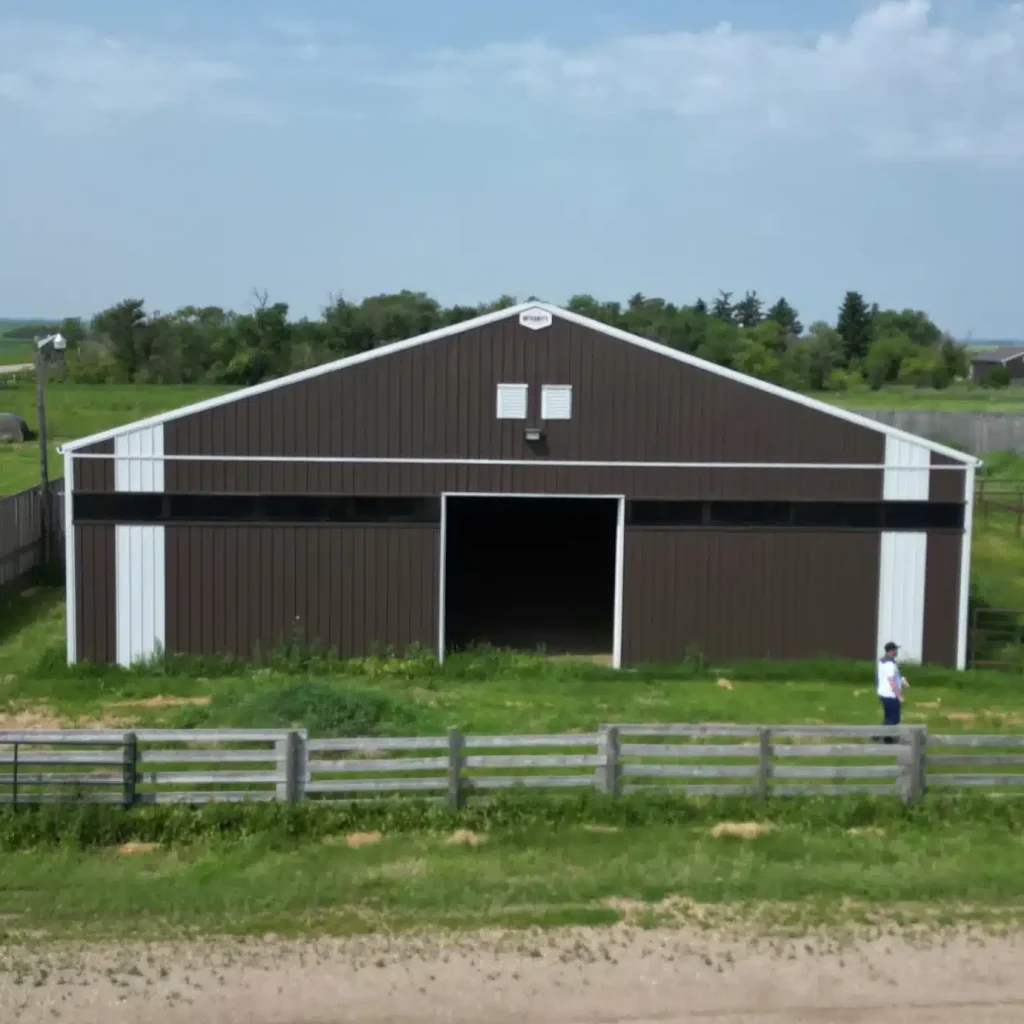 A coffee brown post-frame livestock shelter with overhead and sliding doors