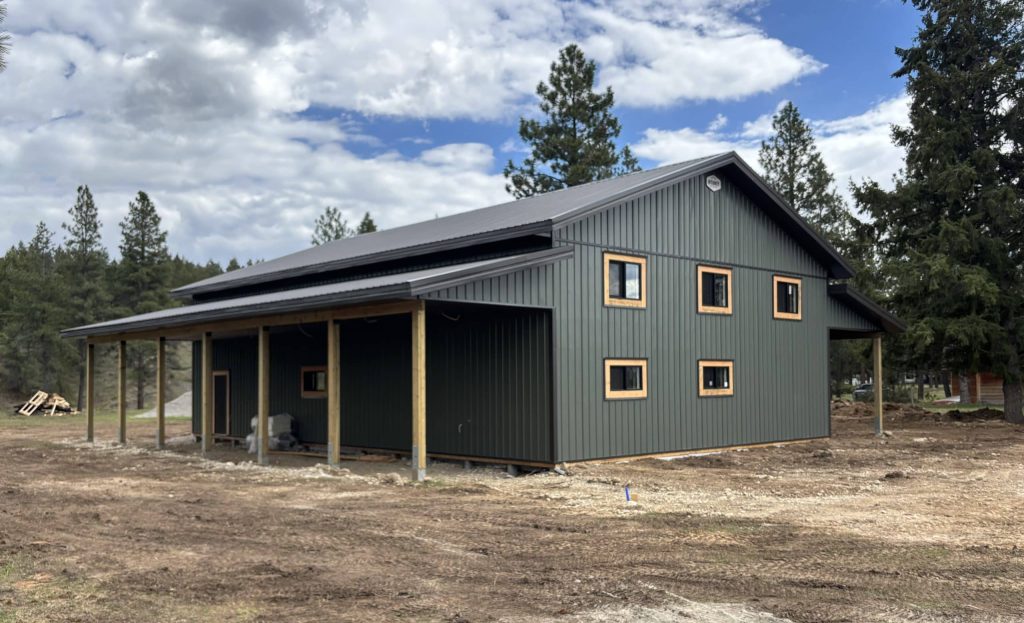 A dark sage post-frame shop with open lean-tos, soffits, and wooden trims