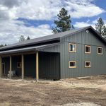A dark sage post-frame shop with open lean-tos, soffits, and wooden trims