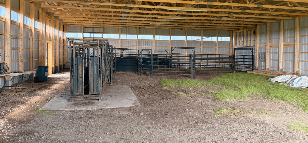 A coffee brown post-frame livestock shelter with overhead and sliding doors